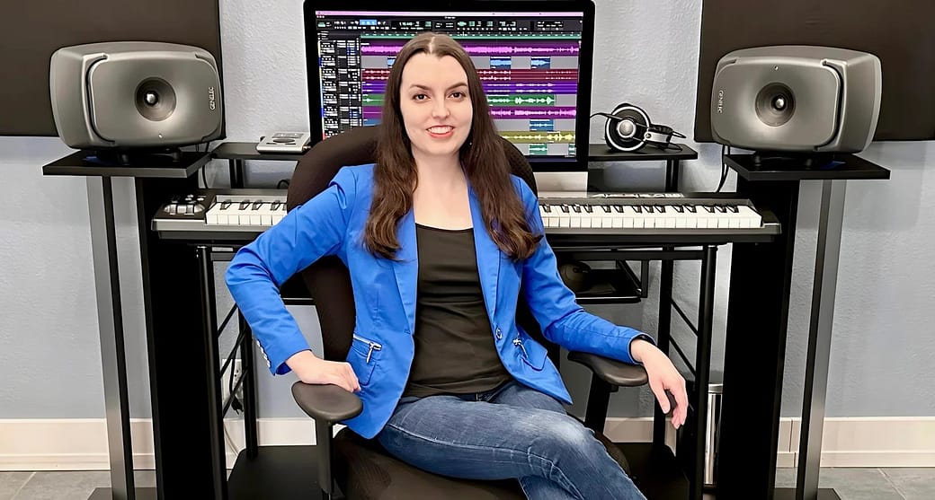 2024 Studio Photo Shelby, a white woman with long brown hair, sitting in front of her mixing desk with Pro Tools on the computers screen and a pair of Genelec 8341A speakers on the desk.