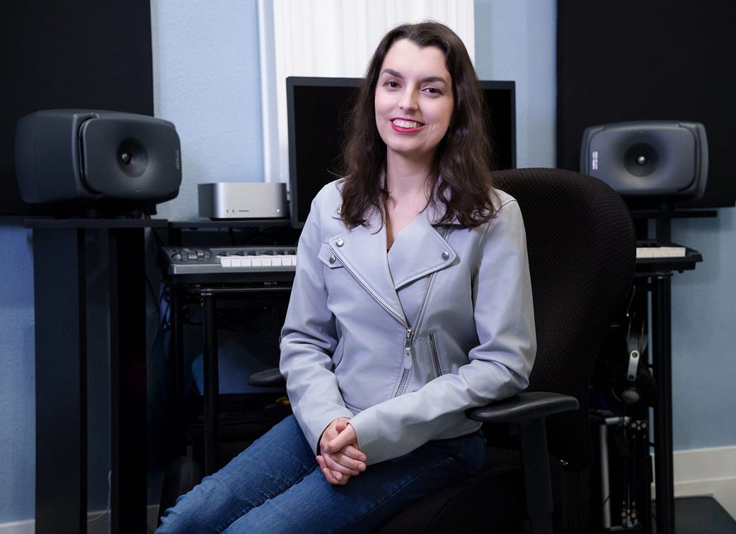 DSC01144-Edit-Edit Shelby Lock, a white woman with long brown hair, sitting in her Santa Cruz recording studio in front of her mixing desk with Genelec 8341A speakers and Mac Studio.